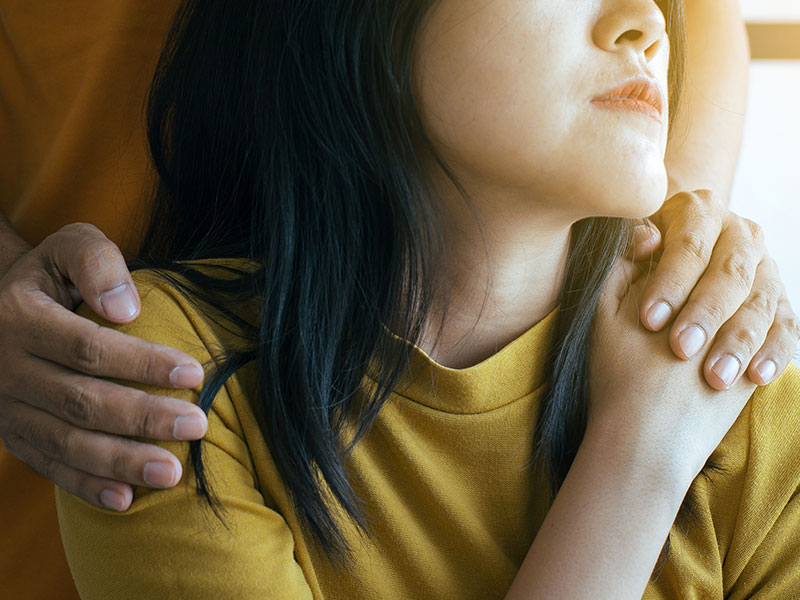 A woman who feels stuck loving a narcissist, sitting with her boyfriend while he puts his hand on her shoulder.