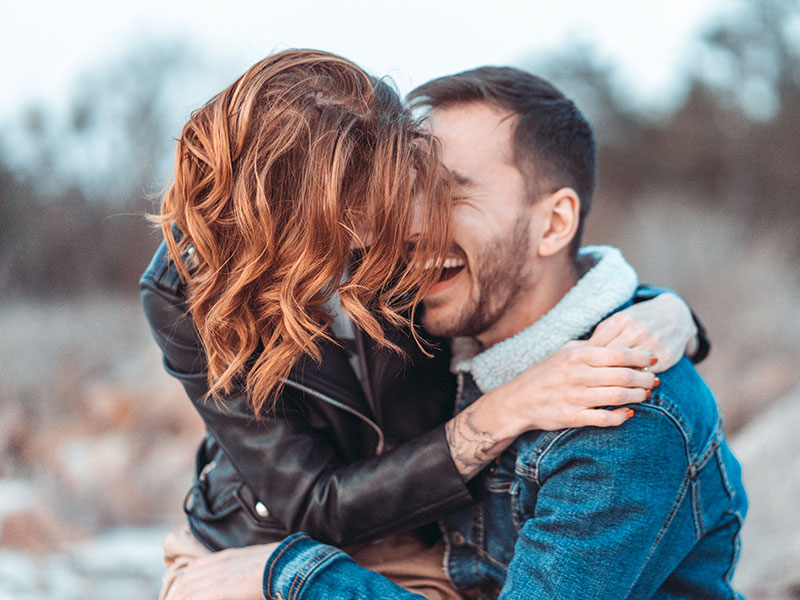 A couple who knows how to have good communication in relationships smiling and laughing outside as they hug.