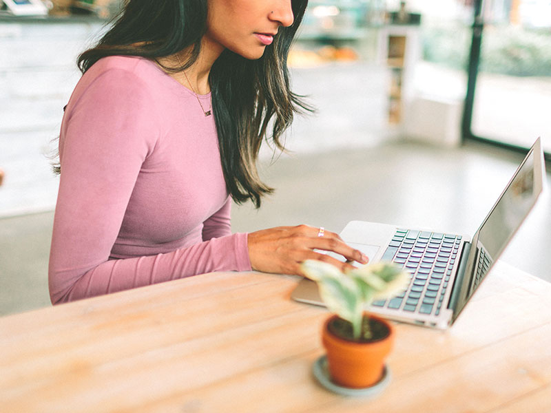 A woman online dating while sitting at her computer in her kitche.