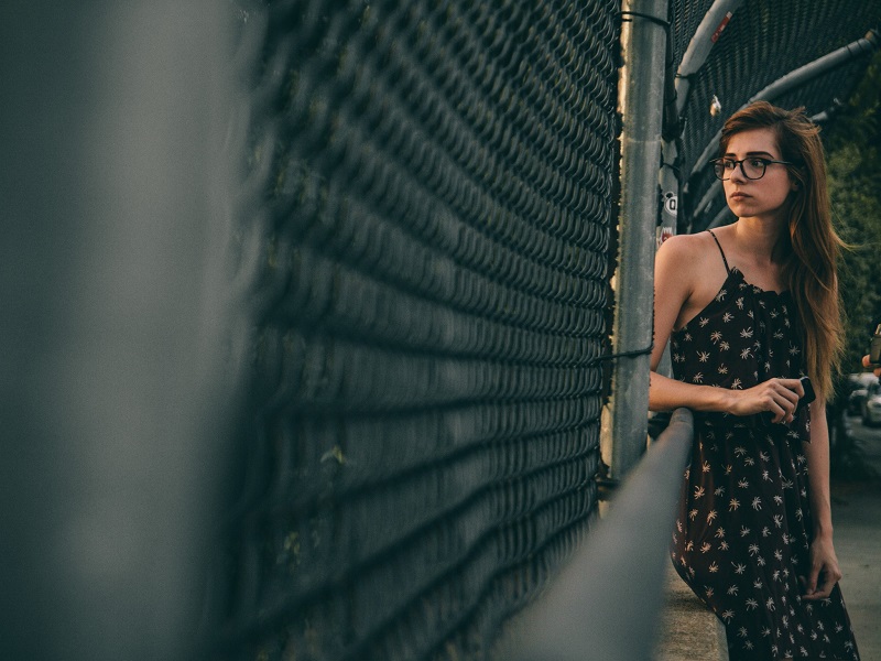 Worried young woman standing by a fence and wondering should I breakup with my boyfriend or not