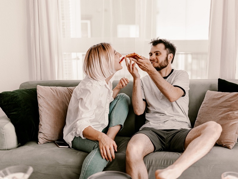 a couple at home on the sofa eating pizza and enjoying quarantine and chill
