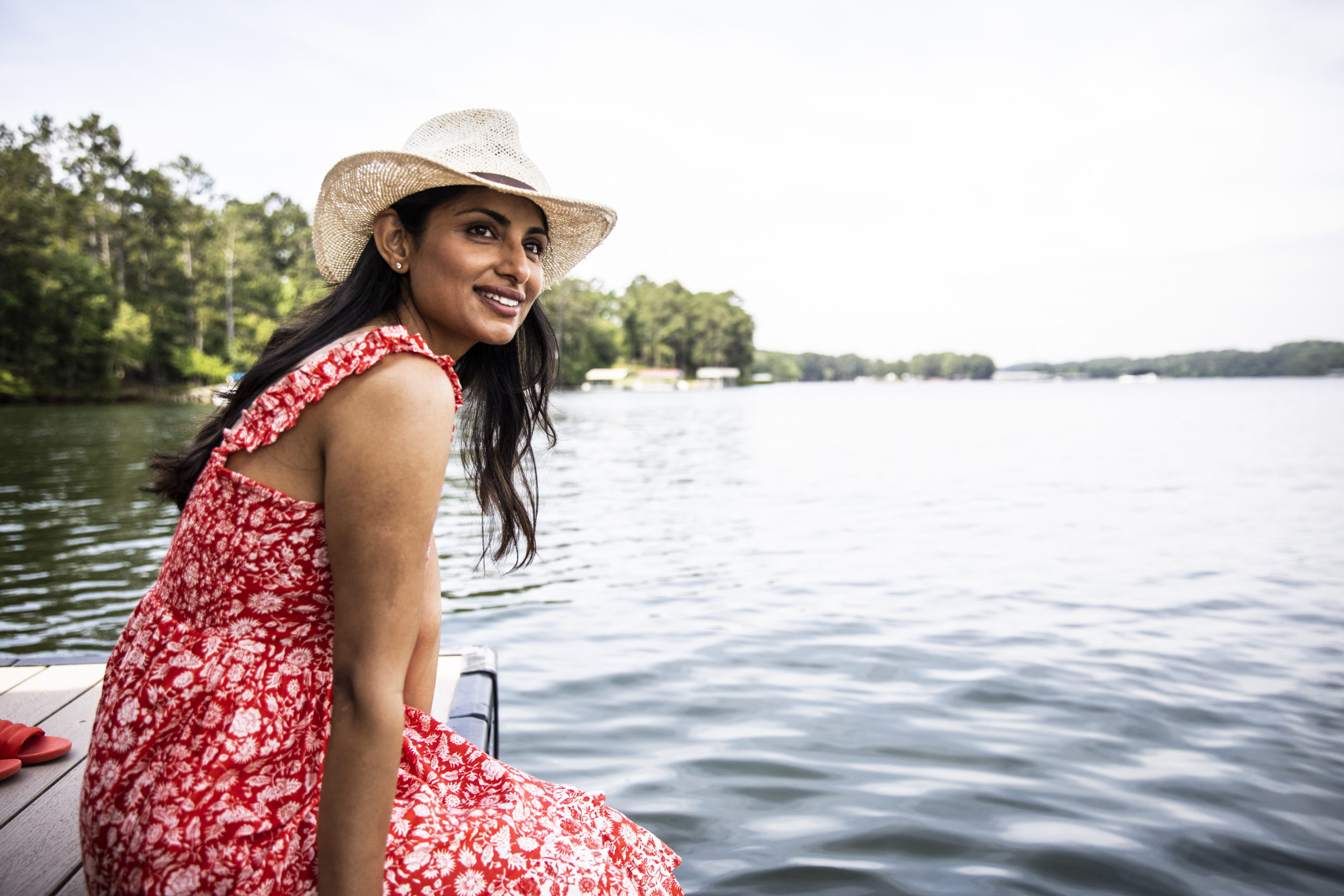 Woman sitting down next to water, smiling and thinking about how to enjoy single life.