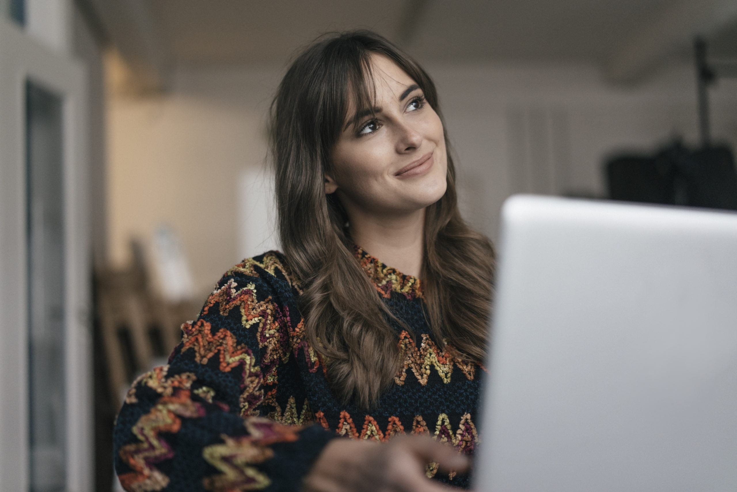 Woman sitting at table in front of laptop, smiling.