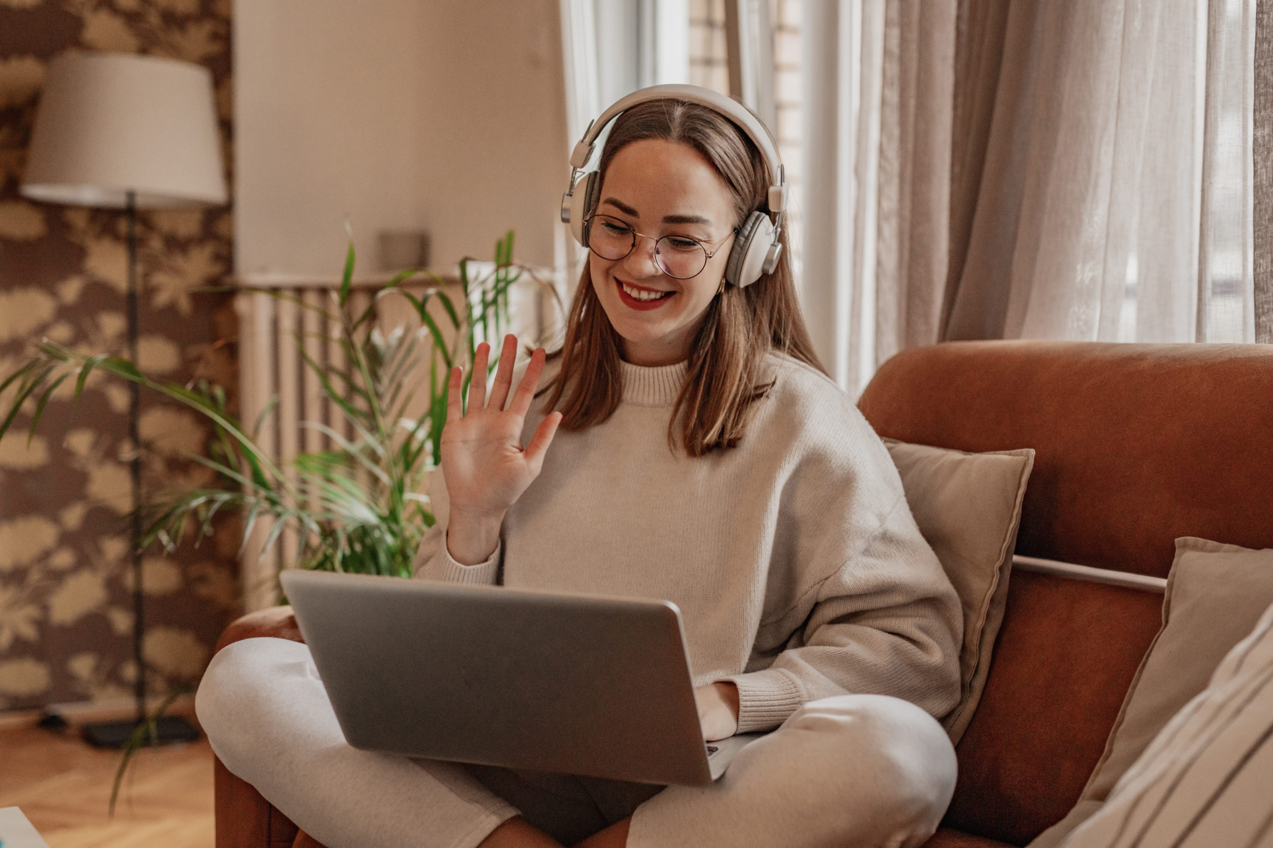 Woman sitting on sofa using laptop and smiling while trying some new online date ideas.