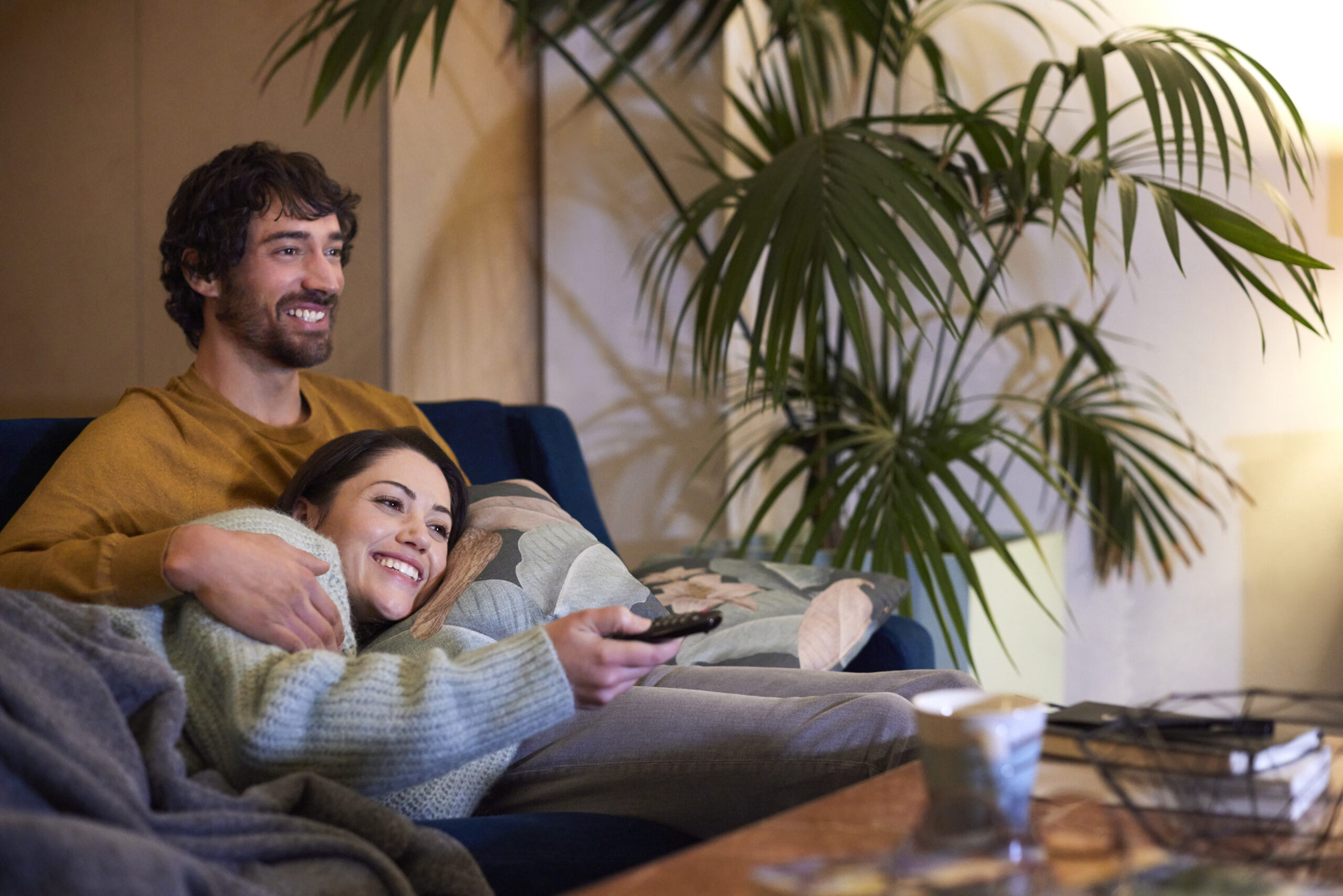 Happy couple smiling and cuddling on the sofa while watching some of the best romantic movies on Netflix.