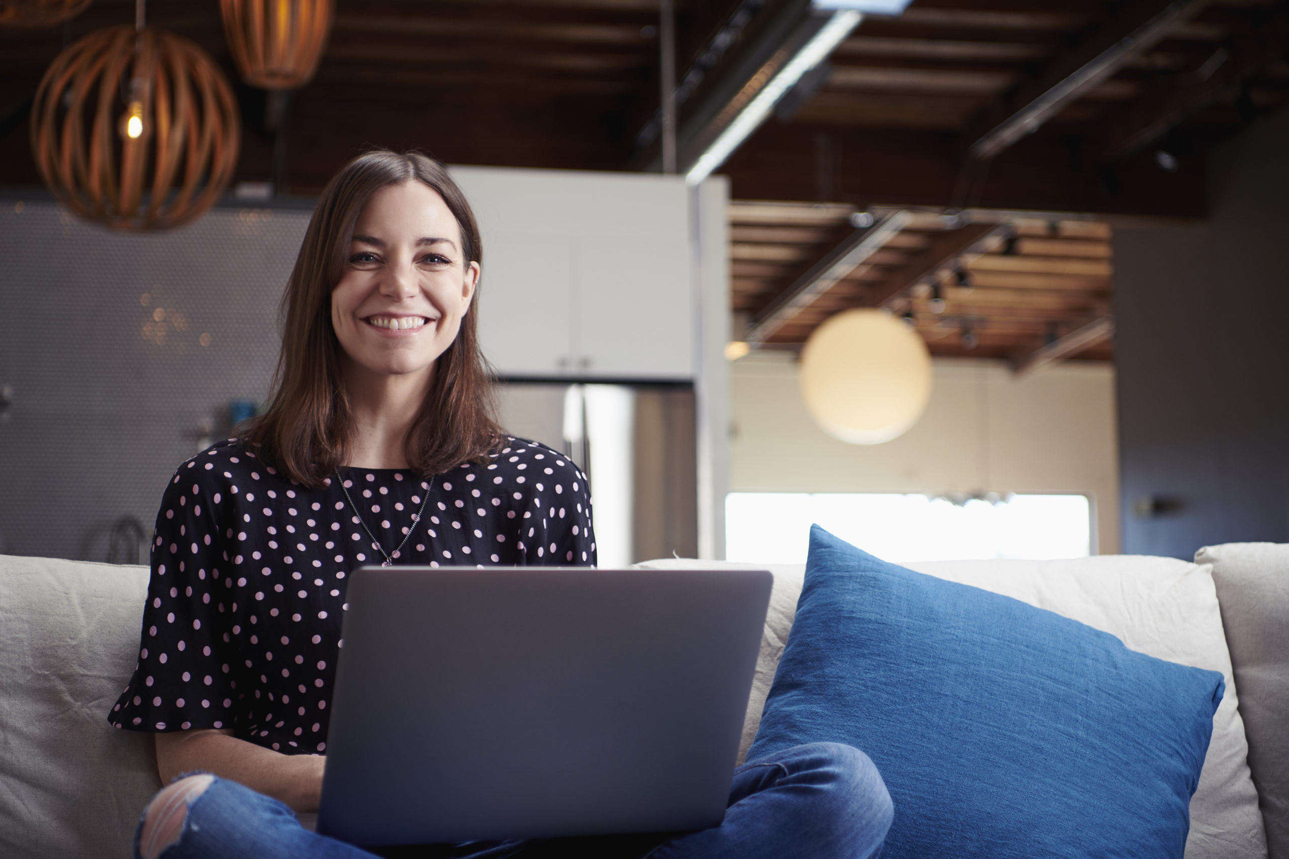 Happy, young woman sitting on sofa using laptop to meet people online while being aware of online dating red flags.