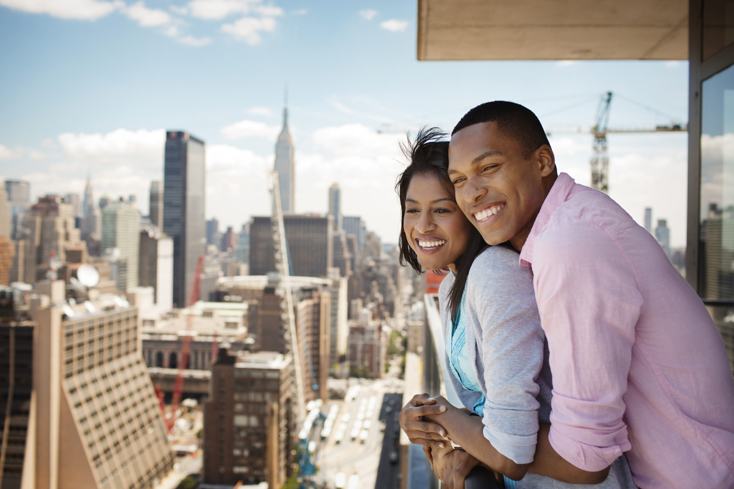 Two happy American singles smiling and embracing each other on a balcony looking over New York City.
