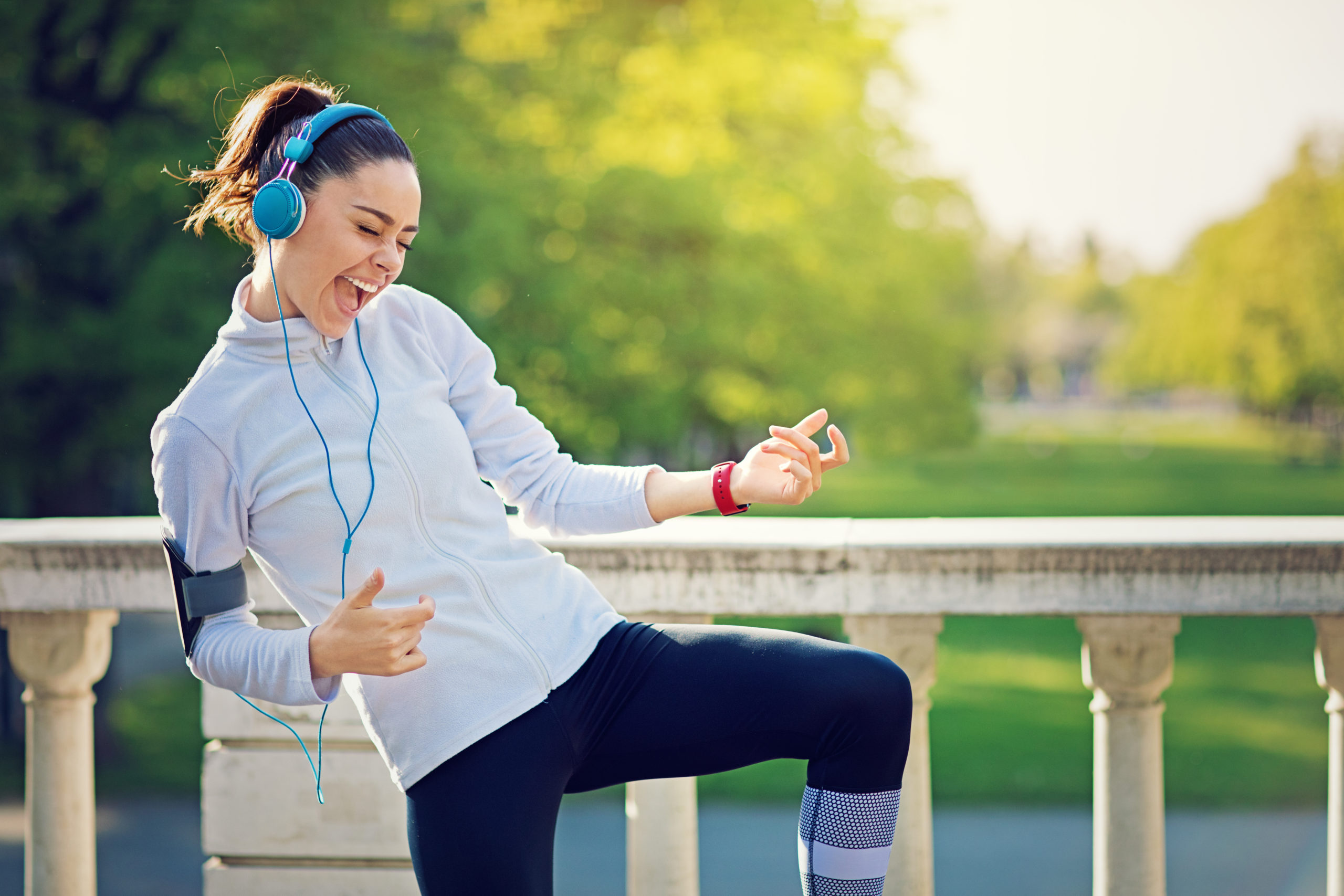 Happy woman wearing headphones and dancing while listening to songs about strong women.