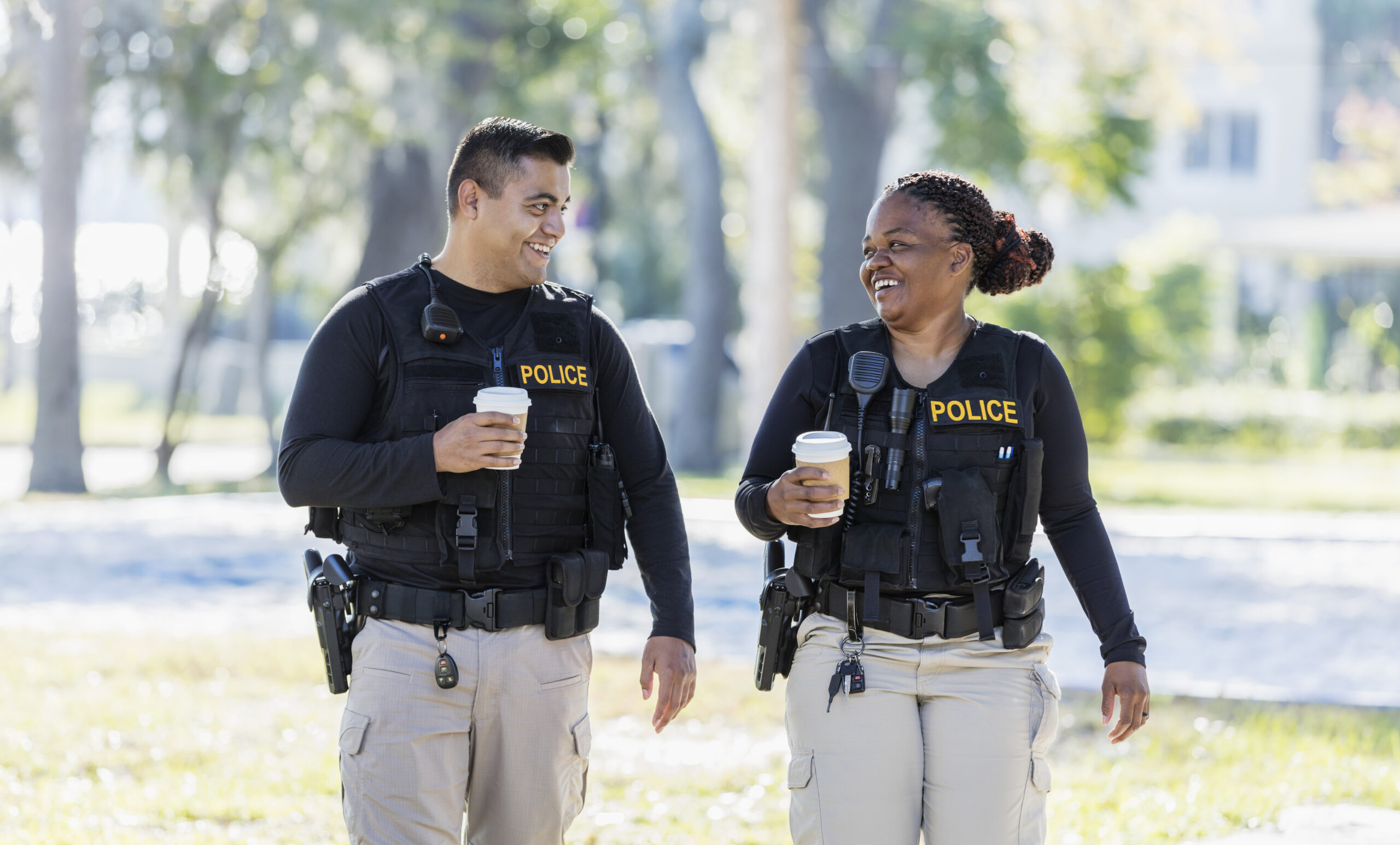 Male and female police officer walking down the street with a coffee and smiling at each other while cop dating.